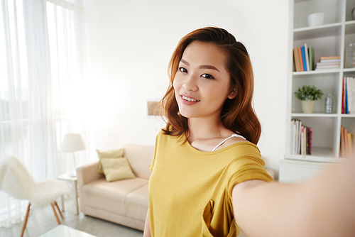 Smiling Asian girl taking selfie on her phone at home