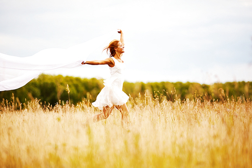 Joyful girl in white dress running in the field