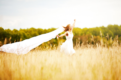 Carefree girl with white chiffon shawl running in the field on summer day