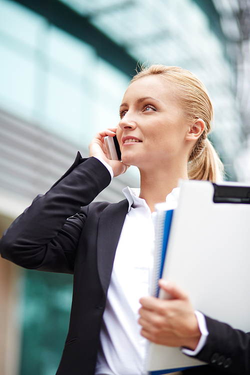 Modern young businesswoman speaking on cellphone outside