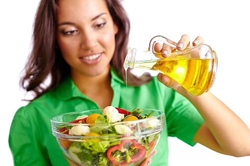 Young woman adding olive oil into just cooked salad