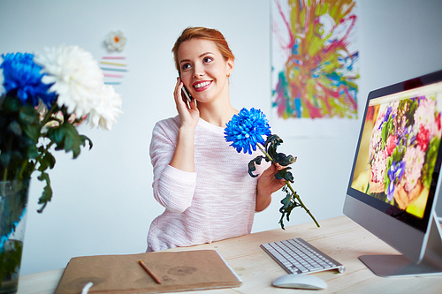 Modern young designer speaking on cellphone in front of computer