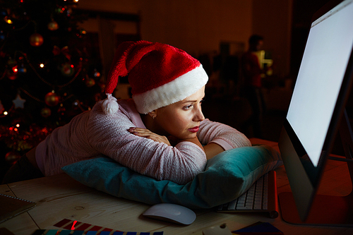 Girl in Santa cap relaxing on pillow in front of computer