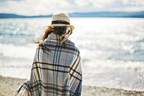 Rear view of a blonde woman warming up in a blanket on the beach