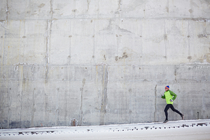 Young sportsman running along concrete wall in winter