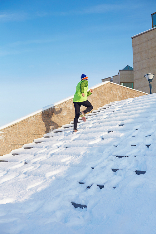 Sportsman jogging upwards on stairs in urban environment in winter
