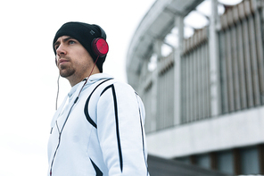 Young sportsman in activewear listening to music in headphones