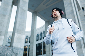Sportsman in activewear jogging on background of edifice
