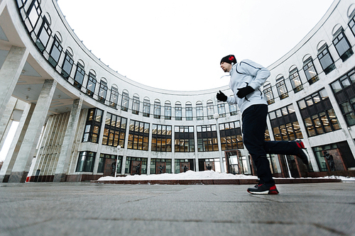 Active young man running in urban environment along institutional building