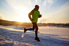 Sportsman running in snowdrift at sundown