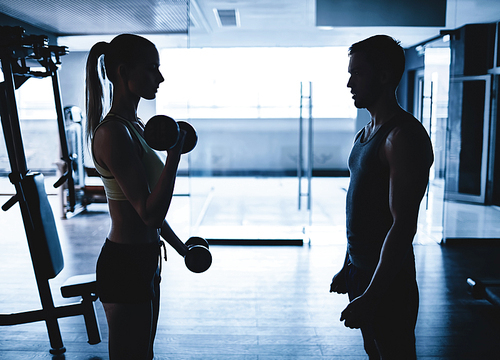 Young woman doing exercise with dumbbells with her trainer near by