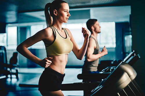 Active female running on treadmill in gym with young man on background