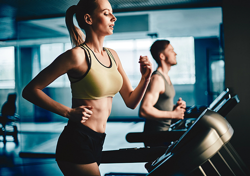 Active young woman running on treadmill with guy on background