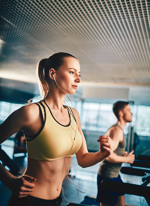 Active woman listening to music while running on treadmill