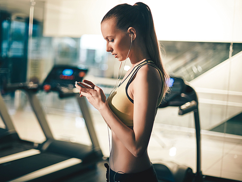 Pretty woman with smartphone listening to music after training in gym