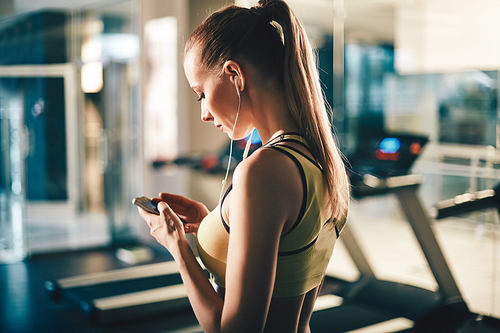 Active girl with smartphone listening to music in gym