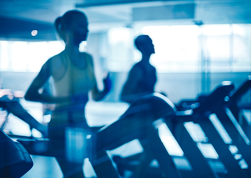 Young man and woman running on treadmills in gym