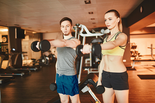 Young man and woman with stretched arms exercising barbells together