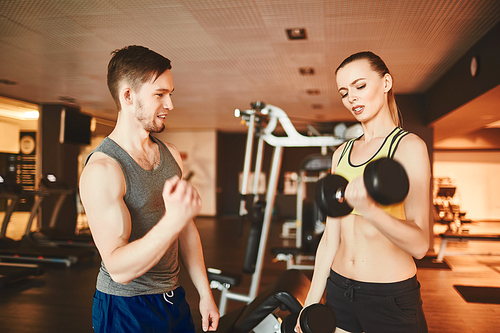 Handsome trainer consulting young female with barbells in sports club