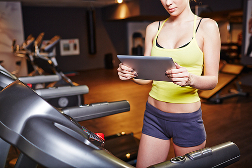 Fit girl in activewear using touchpad while training on sportive equipment