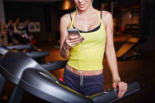 Fit girl with smartphone listening to music in sports club