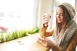 Cute girl in warm knitted clothes using touchpad in cafe