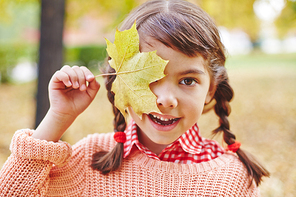 Adorable girl with yellow maple leaf by her eye 