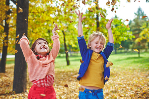 Ecstatic little friends playing with falling leaves in park