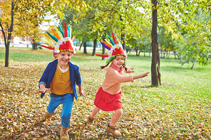 Cute girl and boy in Indian headdresses running in autumn park