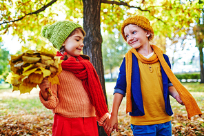 Two cute children in knitted scarves and caps spending leisure in park