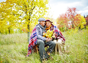 Old man and woman in warm clothes sitting in park at leisure