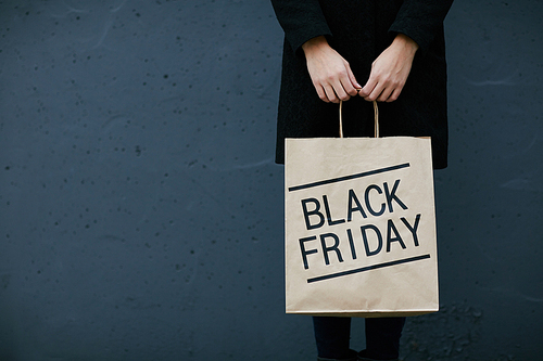 Young woman in black holding paperbag with note Black Friday