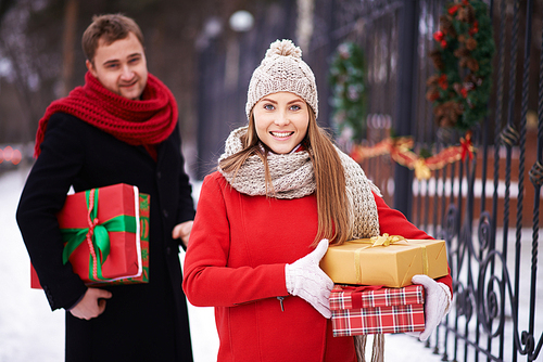 Smiling woman standing with gift boxes with man behind her