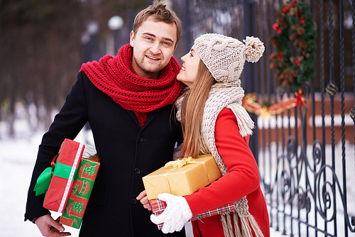 Young woman with giftboxes saying something to her husband outdoors on Christmas eve