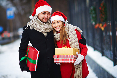 Amorous couple in Santa caps holding giftboxes