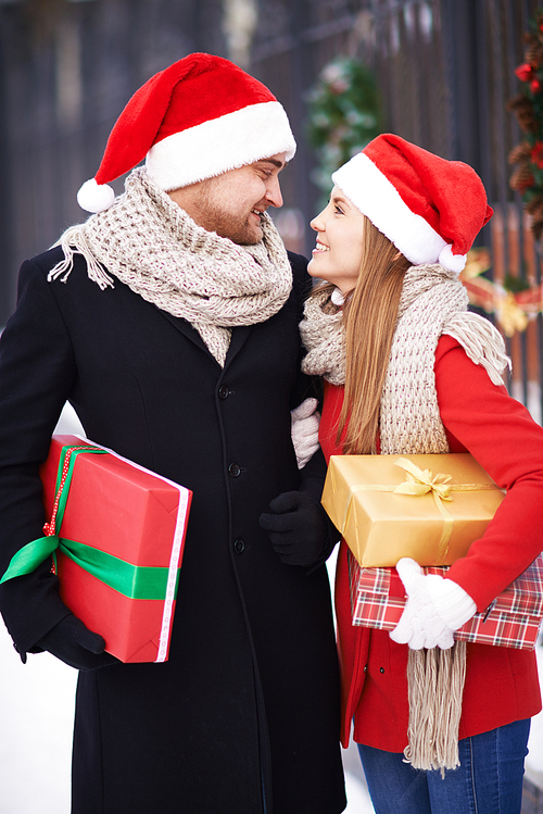 Amorous couple in Santa caps and coats holding presents for Christmas