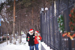 Happy couple in Santa hats with Christmas gifts walking outdoors