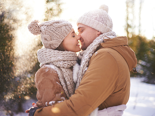 Young amorous couple in winterwear going to kiss