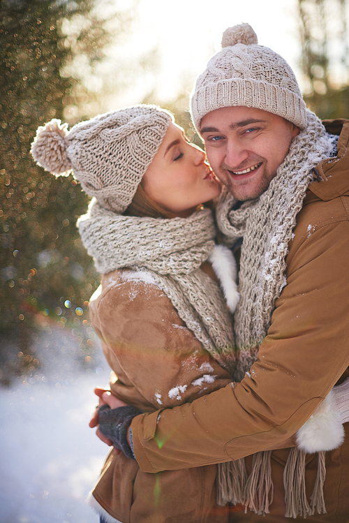 Amorous young woman kissing her happy boyfriend on winter day