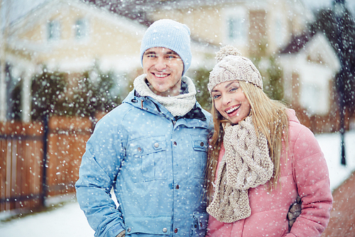 Winter young couple standing while it’s snowing