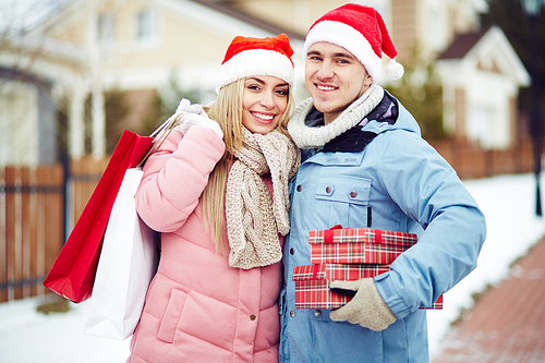 Young couple in Santa Claus hats holding gifts