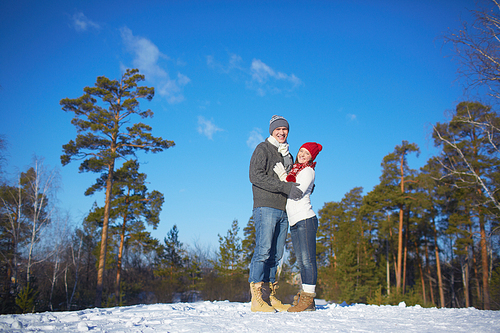 Affectionate couple in knitted winterwear enjoying weekend in forest