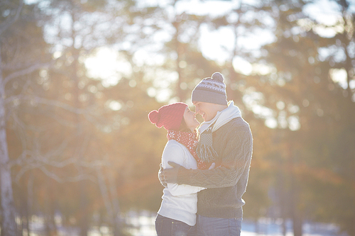 Cheerful couple in knitted winterwear embracing outdoors