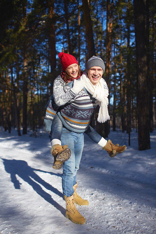 Joyful couple in knitted winterwear having fun in winter forest