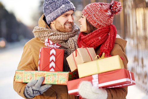 Amorous couple with gift-boxes looking at one another outdoors