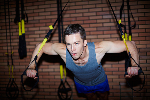 Young man in activewear strengthening arm muscles on special facilities