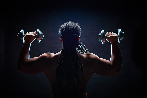 Muscular man lifting dumbbells against black background
