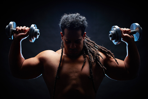Strong and active young man with dreadlocks working out with barbells
