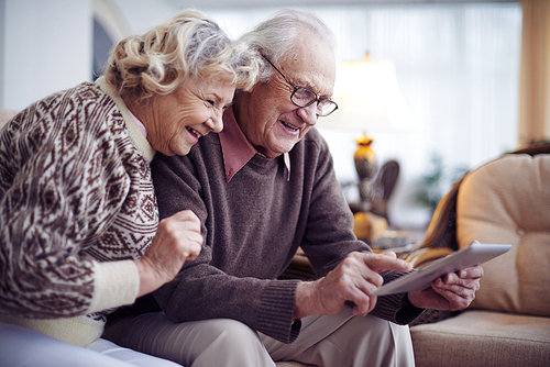 Happy aged couple with touchpad networking at home
