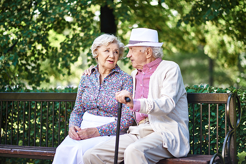 Senior couple in smart casual sitting on bench in park and interacting